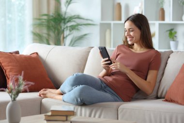 Teras renginde mutlu bir kadın evdeki koltukta cep telefonu kullanıyor.