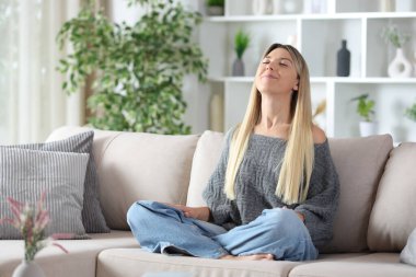 Tatmin olmuş, meditasyon yapan ve temiz hava soluyan bir kadın evdeki koltukta oturuyor.
