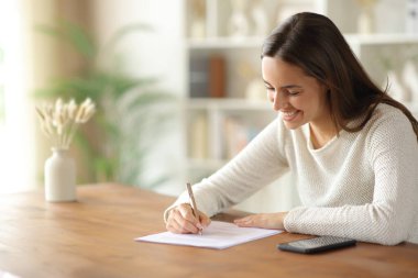 Evdeki ahşap masada kağıt form dolduran mutlu kadın.