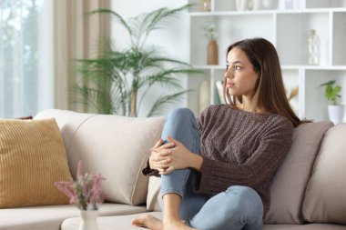 Ciddi bir kadın evdeki kanepede oturup düşünüyor ve kafasını çeviriyor.