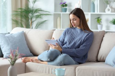 Mavili ciddi bir kadın not defterine not alıyor. Evdeki kanepede oturuyor.