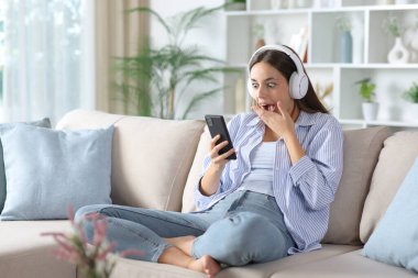 Mavili, kulaklık takan, telefonunu kontrol eden, evdeki koltukta oturan sürpriz bir kadın.