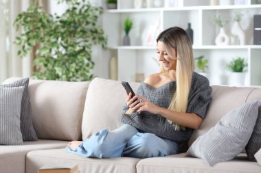 Mutlu kadın evdeki koltukta oturup akıllı telefon kullanmaktan zevk alıyor.