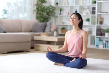 Mutlu Asyalı kadın evdeki halıda yoga egzersizi yapıyor.