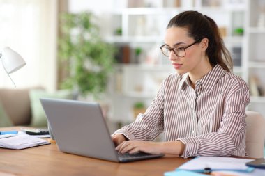 Evde dizüstü bilgisayar kullanarak çalışan gözlüklü bir telgraf çalışanı.