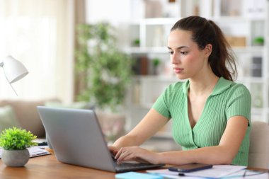 Evde çalışan, laptopta yazan yeşil işçiyle ilgili ciddi bir serbest çalışma.