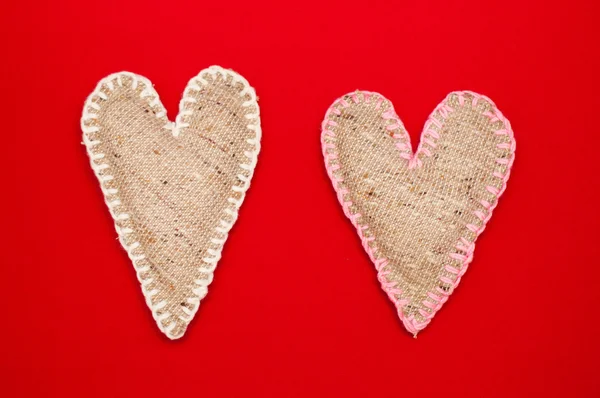 Dos corazones de lino hechos a sí mismos sobre fondo rojo — Foto de Stock