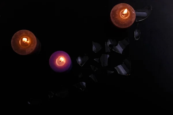 Love triangle and broken relationship concept. Broken glass and three burning candles on black background. Flat lay, top view, place for text.