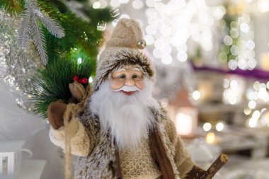 Kahverengi giyinmiş Noel Baba oyuncağı. Yeni yıl dekorasyonu, yılbaşı ışıl ışıl ışıkları ve odaklanmamış arka planda bokeh. Kış tatili sahnesi, mucize bekliyor..