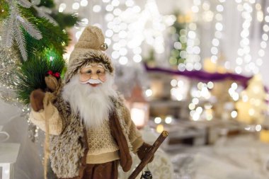Kahverengi giyinmiş Noel Baba oyuncağı. Yeni yıl dekorasyonu, yılbaşı ışıl ışıl ışıkları ve odaklanmamış arka planda bokeh. Kış tatili sahnesi, mucize bekliyor..