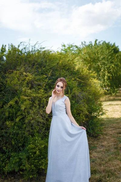 Beautiful girl in tender prom dress on green bush background. Female portrait on spring landscape.