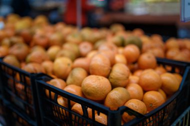 Marketteki, süpermarketteki, alışveriş merkezindeki, hipermarketteki ya da alışveriş merkezindeki meyve reyonunun yumuşak odaklı görüntüsü. Portakal ve mandalinalı kutular, arka planda tanınmayan insanlar. Sağlıklı beslenme, Noel konsepti.