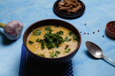 Bir kase bezelye ya da mercimek çorbası taze maydanoz, sarımsak, aromatik biber seti ve mavi ahşap arka planda çavdar ekmeği krakeri ile servis edilir. Sağlıklı beslenme.