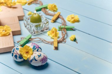 Süslü Paskalya yumurtaları, sarı çiçekler, yanan mumlar ve ahşap mavi arka planda kahverengi tahtalar. Bahar ve Paskalya konsepti. Kapat, boşluğu kopyala.