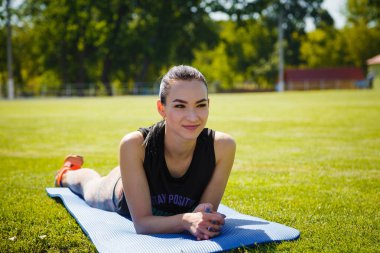 Spor elbiseli genç kız stadyumun yeşil çimlerinde yoga minderinde yatıyor. Spor, sağlıklı yaşam biçimi, spor konsepti..