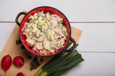 Turp, yeşil soğan, maydanoz, kırmızı kasede yumurta salatası. Mutfakta biraz taze sebze ve yeşillik beyaz ahşap arka planda tahta doğrama. Üst görünüm, alanı kopyala.