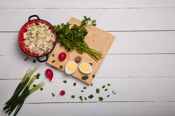 Turp, yeşil soğan, maydanoz, kırmızı kasede yumurta salatası. Mutfakta biraz taze sebze ve yeşillik beyaz ahşap arka planda tahta doğrama. Üst görünüm, alanı kopyala.