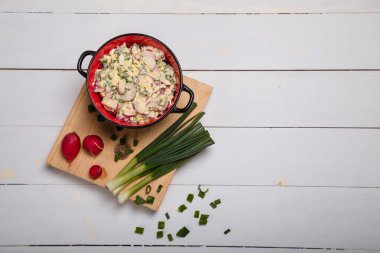 Turp, yeşil soğan, maydanoz, beyaz ahşap arka planda kırmızı kasede yumurta salatası. Sağlıklı yeme alışkanlıkları, organik yiyecekler, diyet ve beslenme konsepti. Üst görünüm, alanı kopyala.