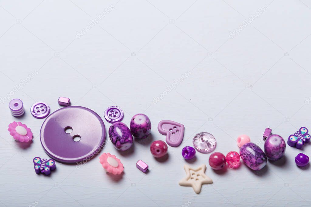 Close up shot of beads and buttons for sewing and embroidery. Purple set of materials for handcraft, making of bijouterie and accessories. White background, copy space.