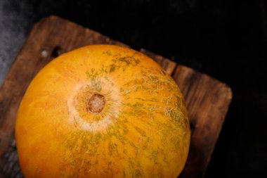 Mutfak tahtasındaki tatlı, sarı kavun, siyah arka plan. Organik mevsimlik tarım meyveleri konsepti. Sağlıklı vejetaryen yemeği. Boşluğu kopyala.