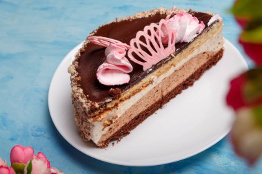 Pastanın yarısı beyaz tabakta, mavi tabakta. Yapay bahar çiçekleri olan tatlı bir fırın