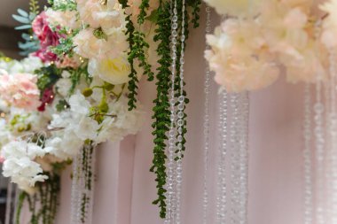 Yumuşak odaklı yapay çiçekler ve pembe arka planda asılı parlak boncuklar. Festival, düğün, yıldönümü ya da doğum günü partisi için süslemeler.