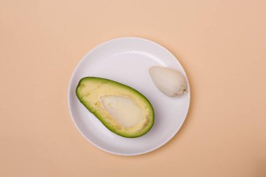 Yeşil taze avokadonun yarısı, bej arka planda beyaz tabakta tohum. Asgari biçimli bileşim.