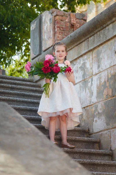 Красивая Маленькая Девочка Белом Платье Стоящая Лестнице Большим Букетом Пионов — стоковое фото