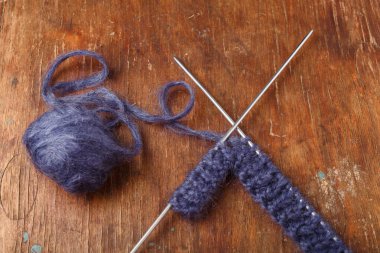 Eski ahşap arka planda örgü iğneleri ve koyu mavi yün yumağı. Örgü örmeye başlıyorum.