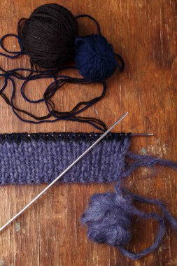 Örgü iğneleri, koyu mavi saç telleri ve eski ahşap masa arkasında siyah akrilik iplik topları. Örgü örmeye başlıyorum..