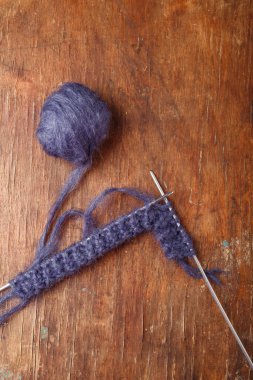 Eski ahşap arka planda örgü iğneleri ve koyu mavi yün yumağı. Örgü örmeye başlıyorum, üst görünüm.