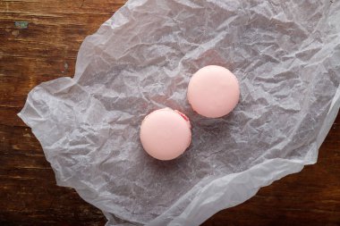 Kağıt üzerinde yumuşak pembe badem kurabiyeleri, ahşap arka plan. Orman meyvesi, çilek ya da ahududu aromalı. Üst görünüm, alanı kopyala.