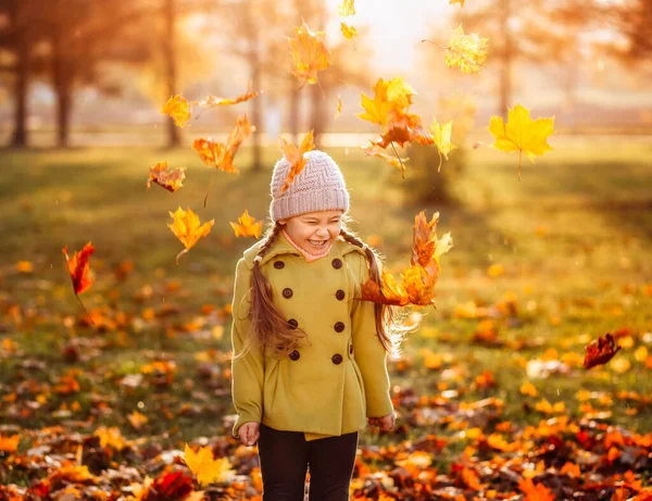 Küçük kız parka sonbahar yaprakları fırlatıyor.