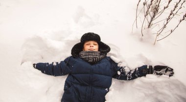 Oğlan karda uzanıyor. Sokakta kış bir kar meleği yapar.