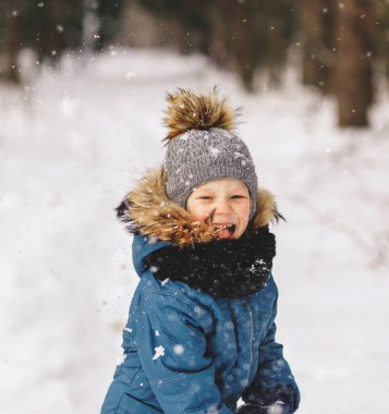 Tatlı çocuk kışın güzel bir kar parkında karla oynuyor.