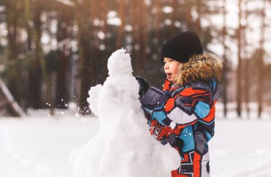 Oğlan güneşli bir günde ormanda kardan adam heykeli yapar.