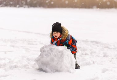 Küçük çocuk kışın parkta bir kartopu yontuyor..