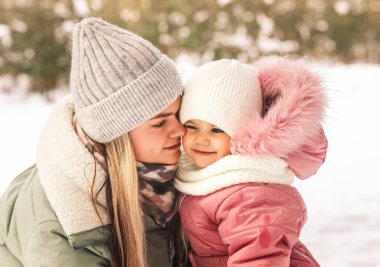 Kışın mutlu bir anne küçük kızını kollarına alır ve ona bakar. Aile fotoğrafı. Annelik ve çocukluk