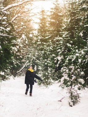 Ergen çocuk kış ormanında eğleniyor ve karla oynuyor. 2021 renginde kıyafetler.