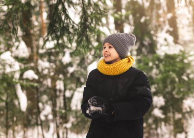 Kış ormanında elinde kartopu olan genç bir çocuk. Moda renginde giyinme