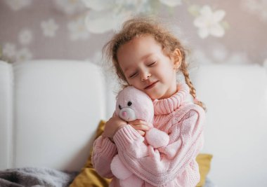 Gözleri kapalı küçük bir kız yatakta yumuşak bir oyuncağa sarılıyor. Şefkat