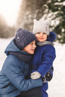Bir erkek kardeş kışın doğada küçük kız kardeşine sarılır. Mutlu çocuklar birlikte