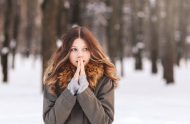 Güzel kız, kışın parkta nefesiyle ellerini ısıtır.