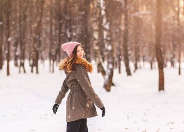Güzel genç kız güneşli bir günde kışın parkta eğleniyor.