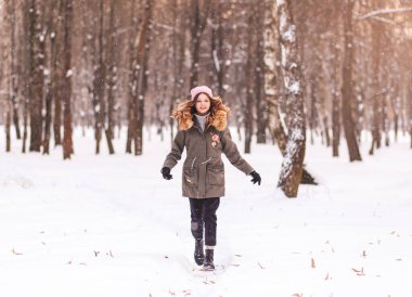 Genç güzel kız kışın parkta karda koşar.