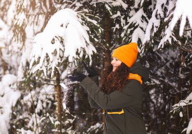 Parlak şapkalı genç bir kız kış ormanında karla oynuyor.