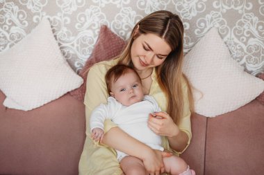 Genç ve güzel bir anne kucağında bir kız bebek koltukta oturuyor.