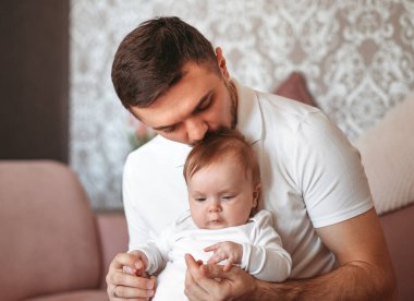 Güzel, genç bir baba, yeni doğmuş kızını bir ışık odasında öpüyor.