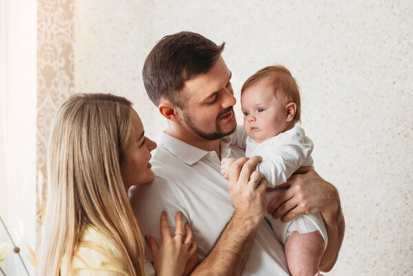 Красивые молодые родители с новорожденной девочкой на руках с нежностью смотрят на свою дочь. Портрет на светлом фоне