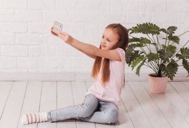 Şirin küçük kız elinde bir akıllı telefon tutuyor ve fotoğraf çekiyor.